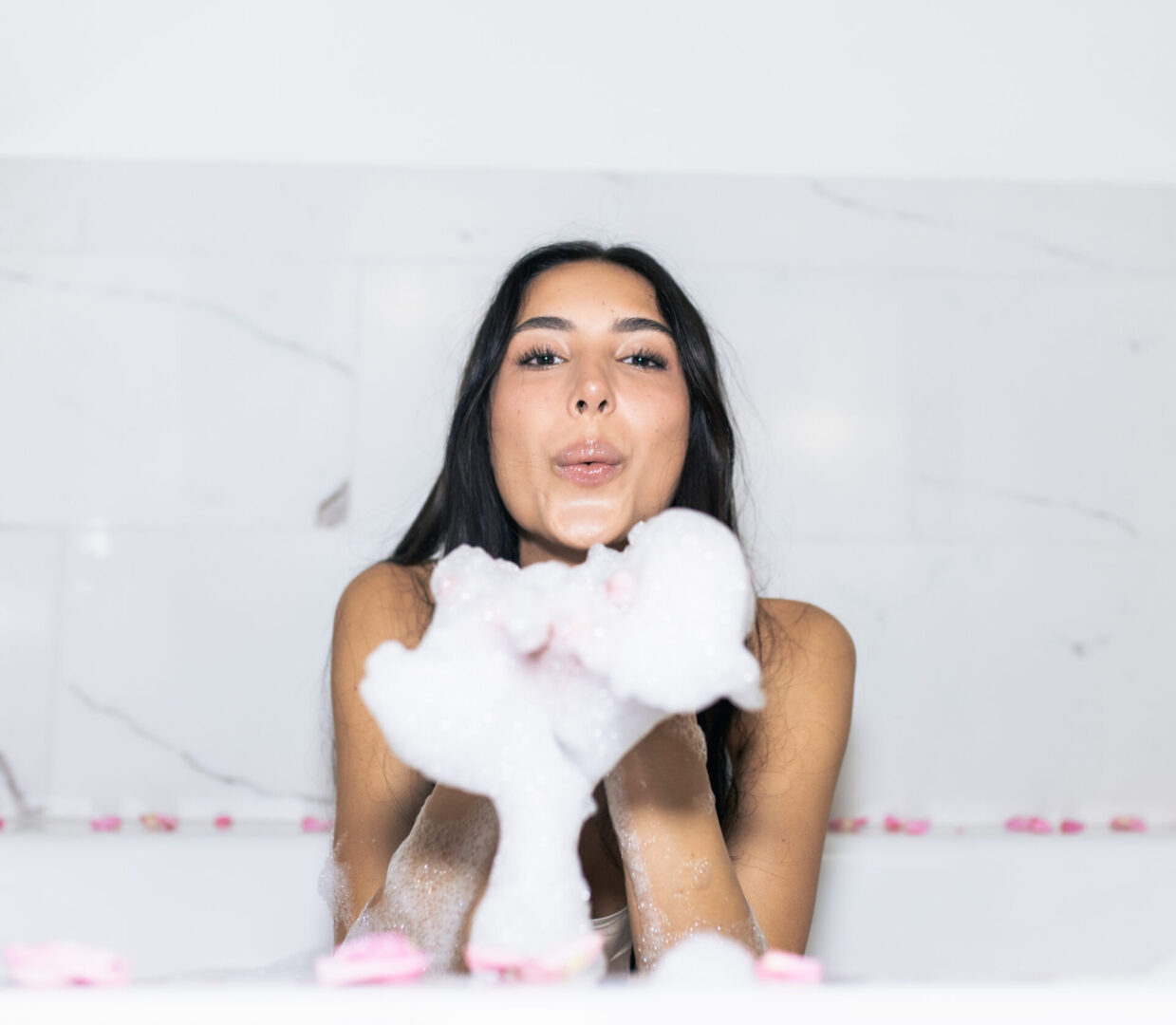 A woman sitting in the tub with her hands up.